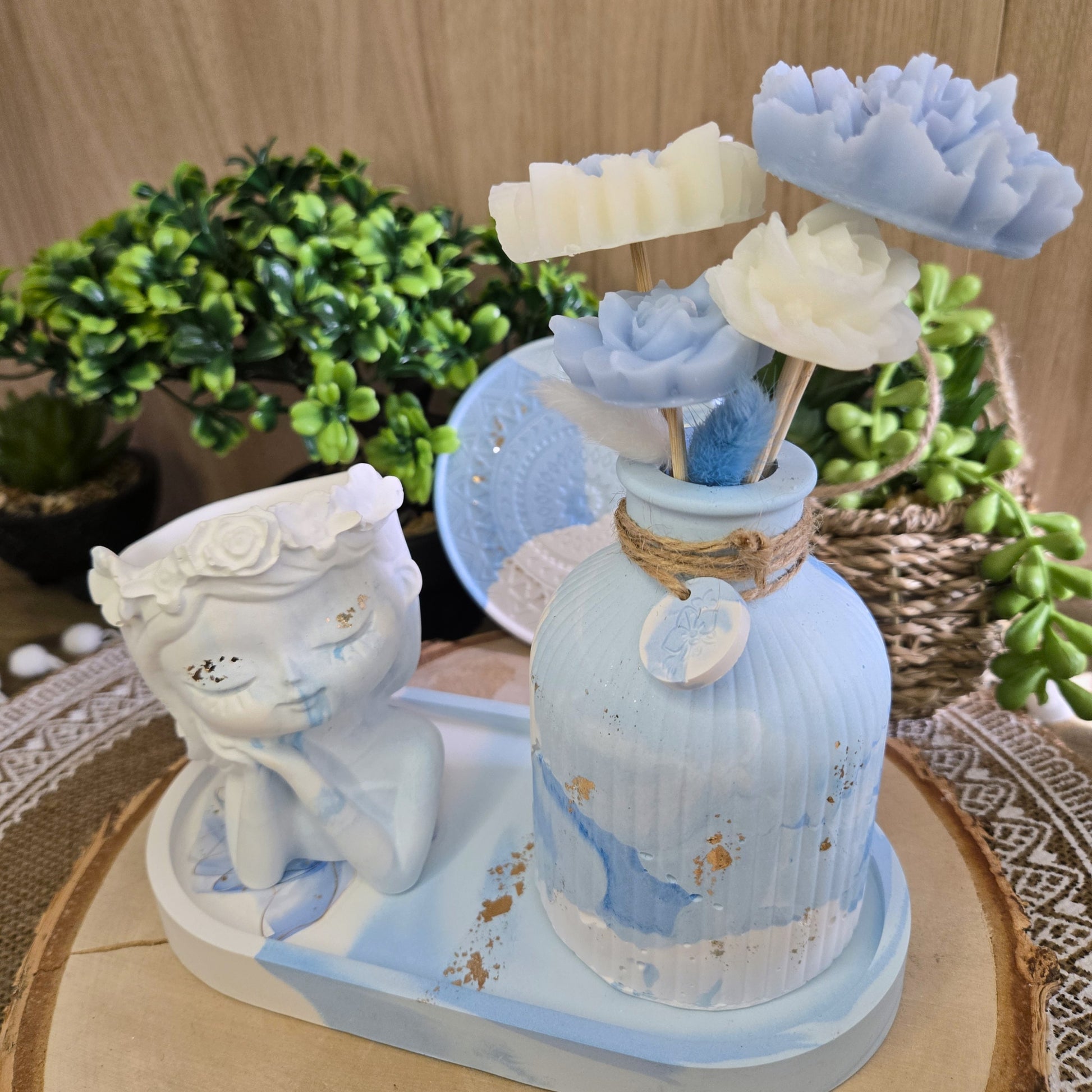 Vue rapprochée du bouquet parfumé en cire végétale coco dans un vase marbré bleu et blanc sur plateau assorti.

