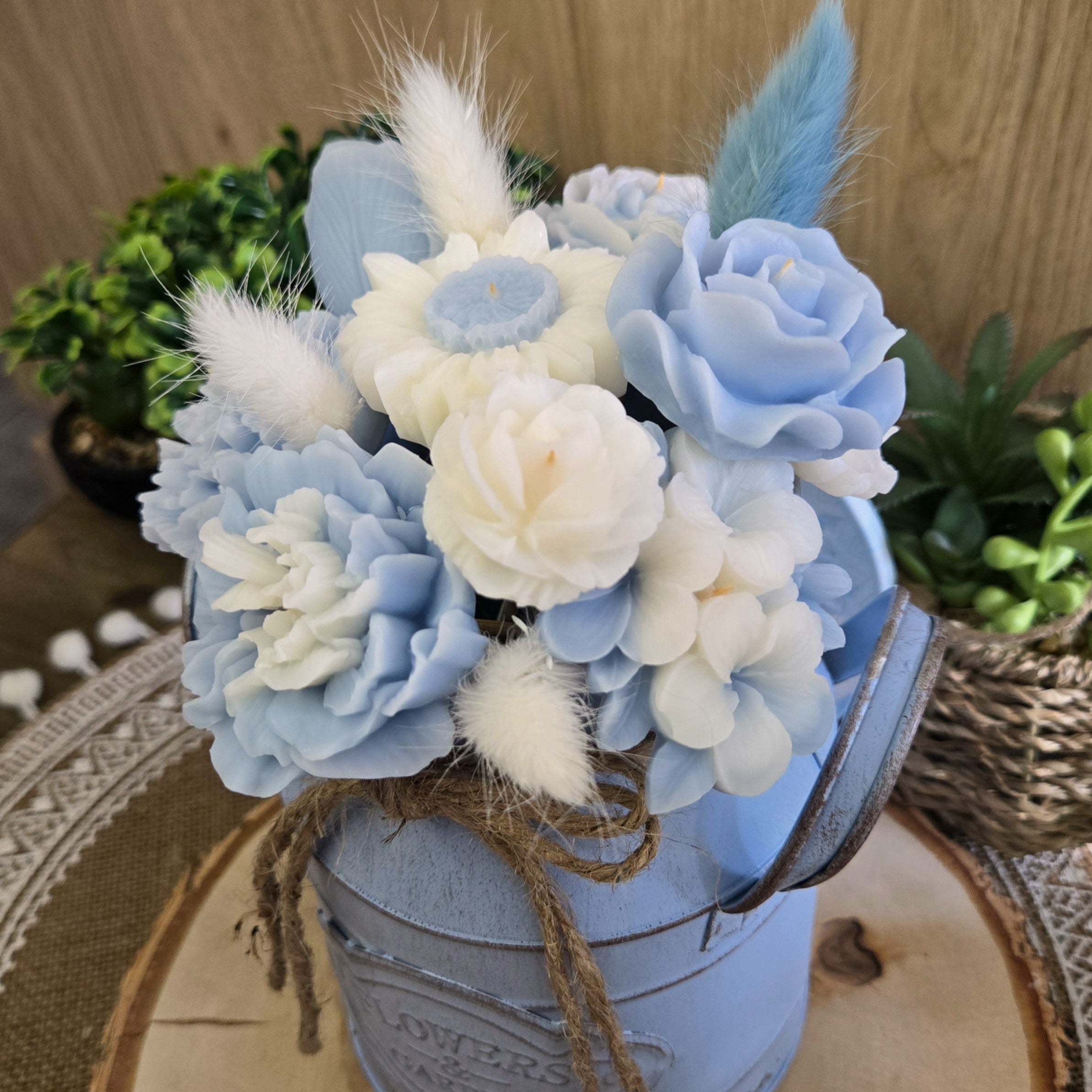 Vue rapprochée du bouquet en cire végétale coco, fleurs artisanales bleues et blanches avec plume décorative.

