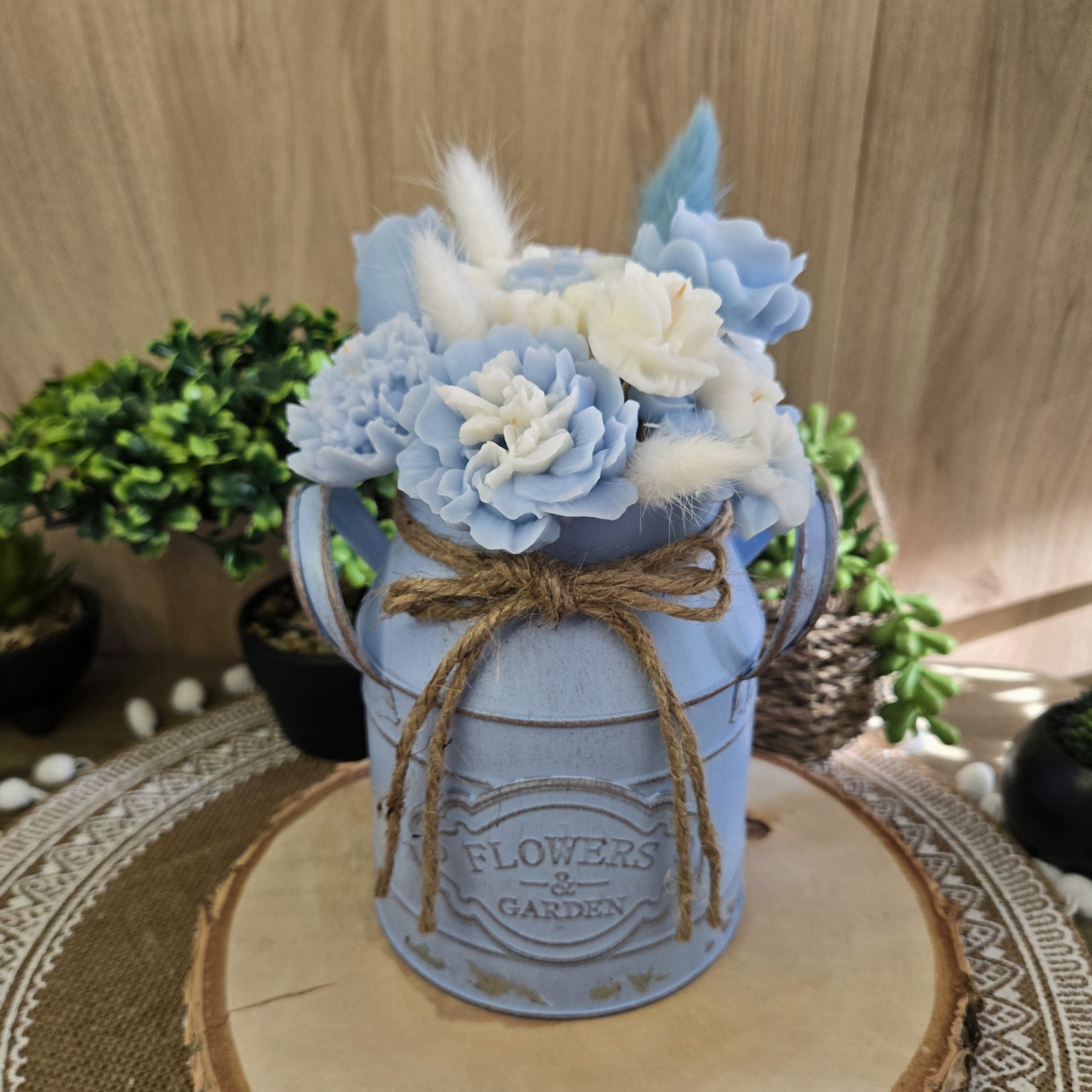 Bouquet parfumé en cire coco tons bleu pastel et blanc, présenté dans un vase bleu vintage sur napperon naturel.

