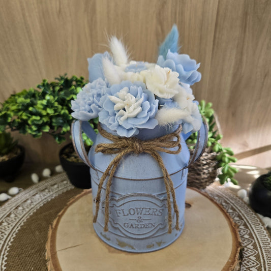 Bouquet parfumé en cire coco tons bleu pastel et blanc, présenté dans un vase bleu vintage sur napperon naturel.

